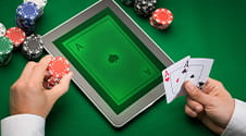 Ein Pokerspieler hält eine Hand, auf dem Tisch liegt ein Tablet.