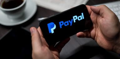 Mann hält Smartphone, auf dem das PayPal Logo zu sehen ist.